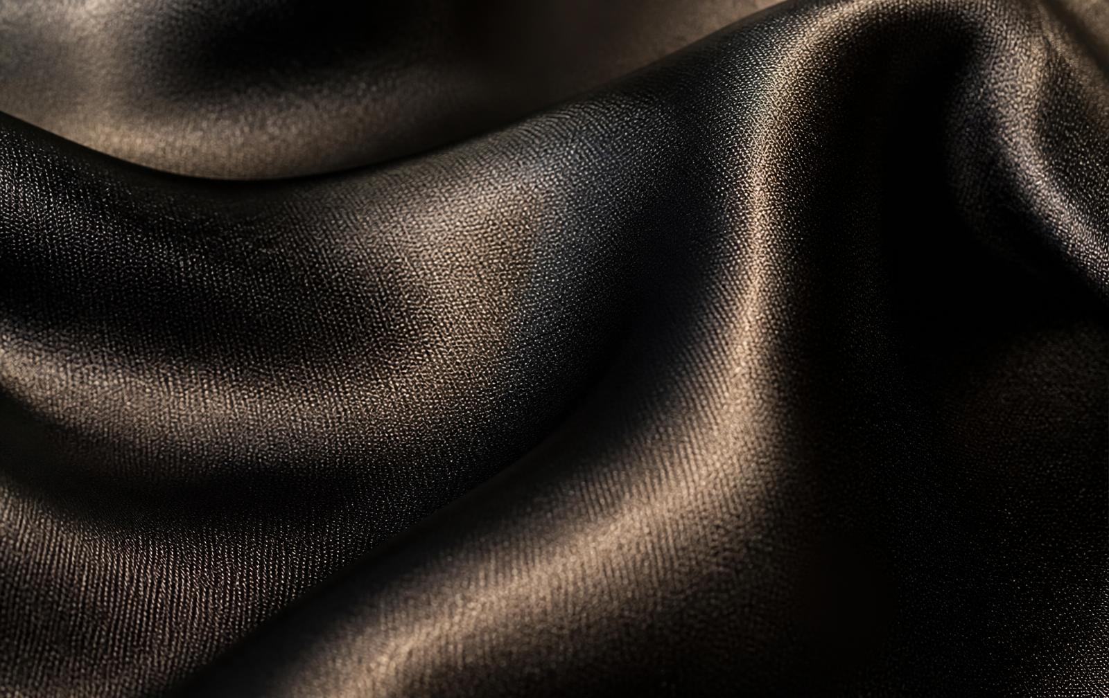 Macro of lustrous black mulberry silk fabric catching warm champagne light.